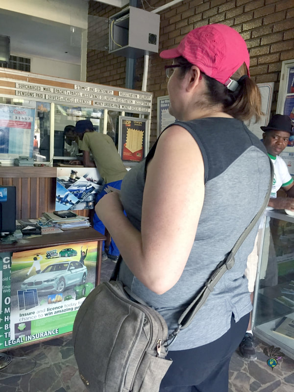 Vanessa standing in a small post office in Zimbabwe while wearing a grey shirt and black pantsPicture