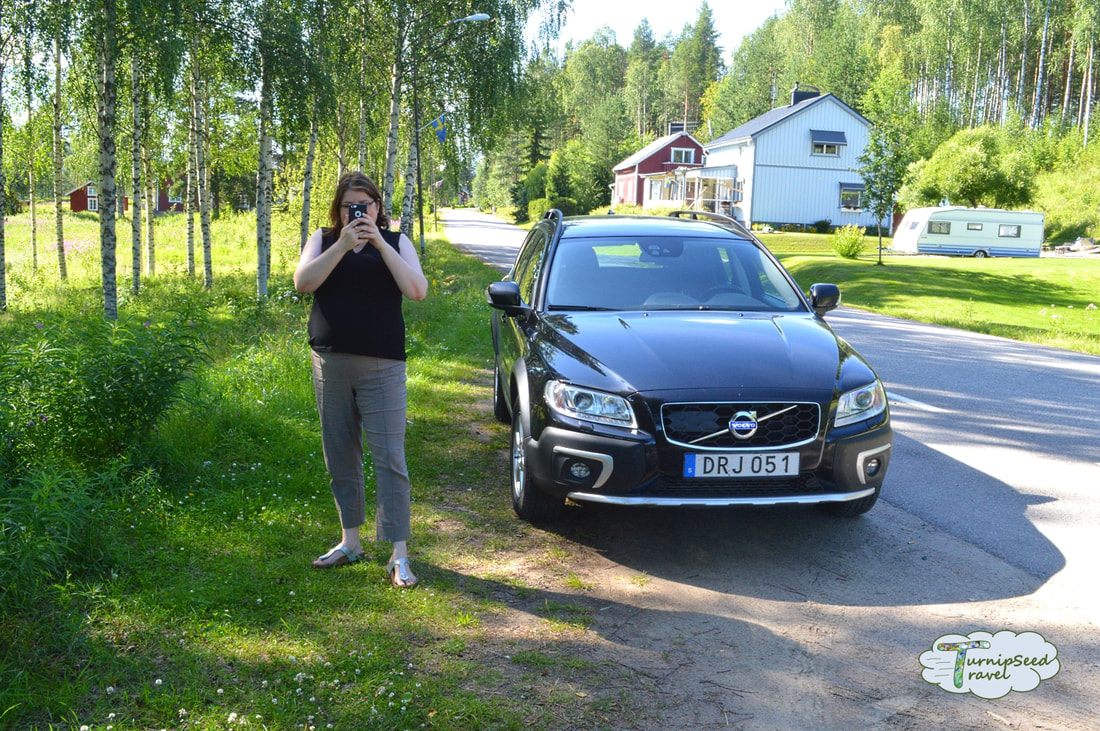 Vanessa takes a photo by a black car in the Swedish countryside