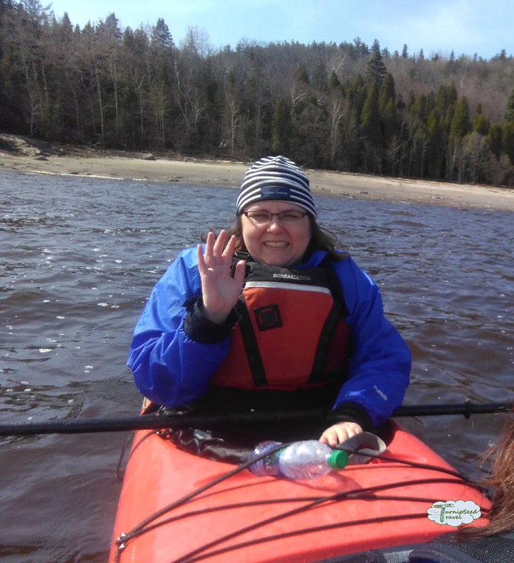 Vanessa wears a blue coat and hat on a red kayak.