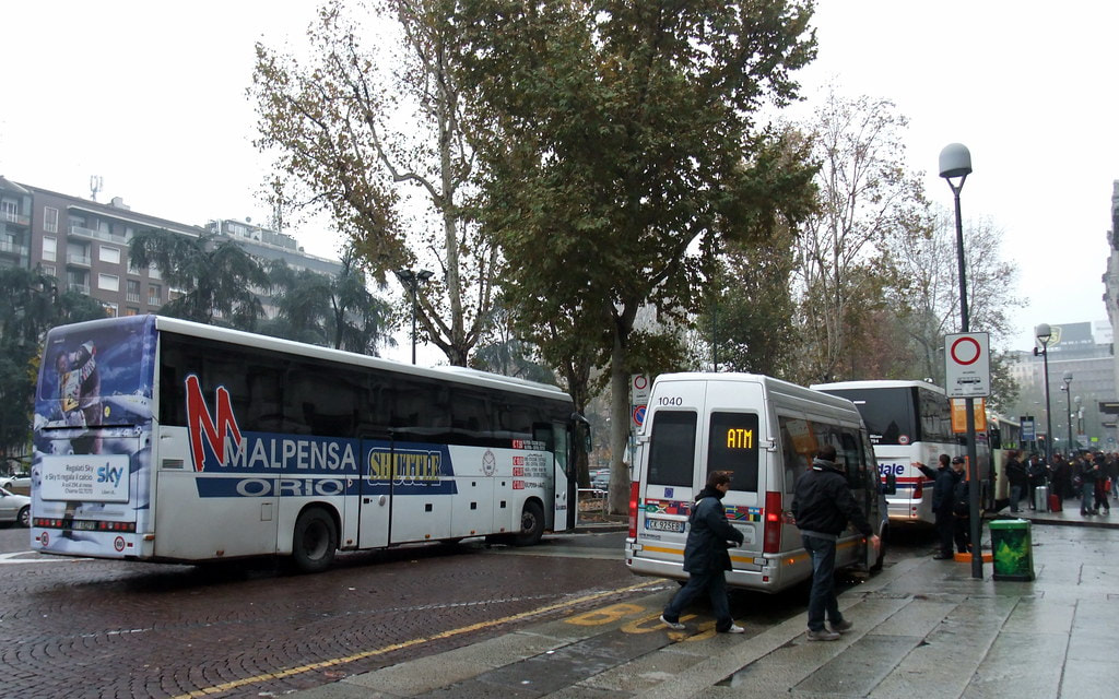 Airport shuttle buses wait in a row on a rainy day in Milan.