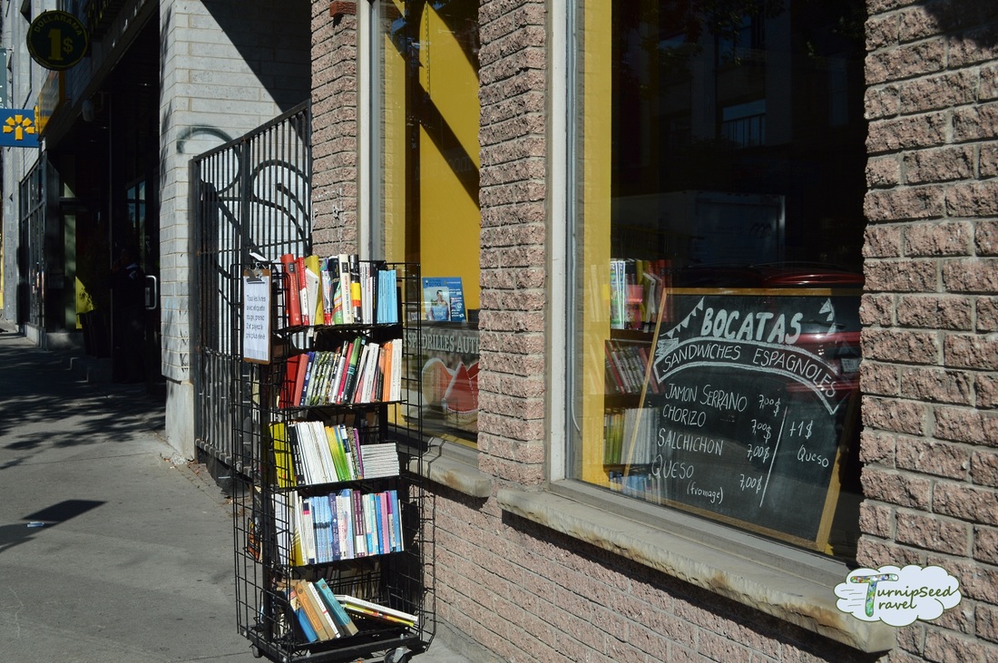 Outside the brick building of the Spanish Library, Montreal with a small rack of books outside and a menu in the windowPicture