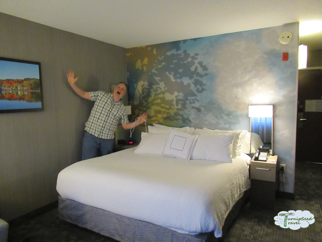 Ryan waves by a hotel bed covered in white linens