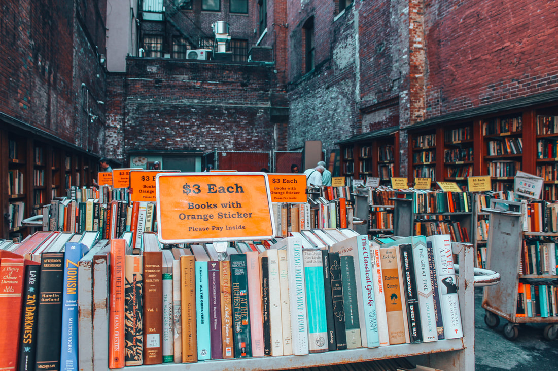 Rows of books sit outside on shelves in an alley lined with red brick buildings Picture