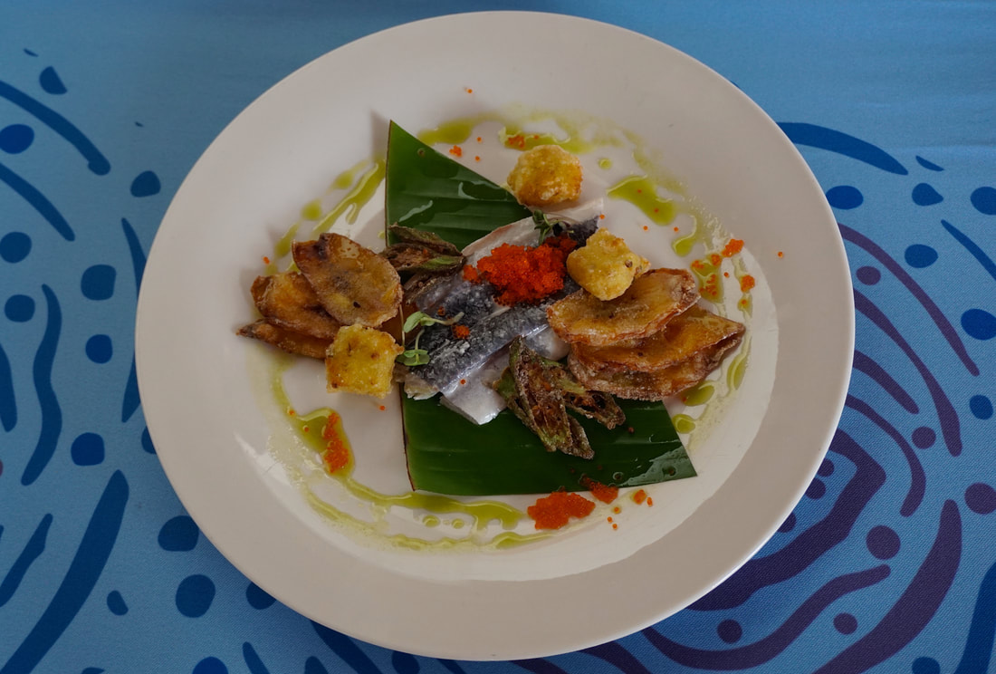 Fried plantain and other food on a white plate covered with a green banana leaf and drizzled with green oilPicture