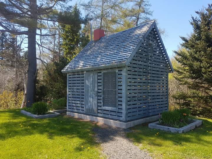 The tiny memorial house built out of grey metal slats, with trees in the backgroundPicture