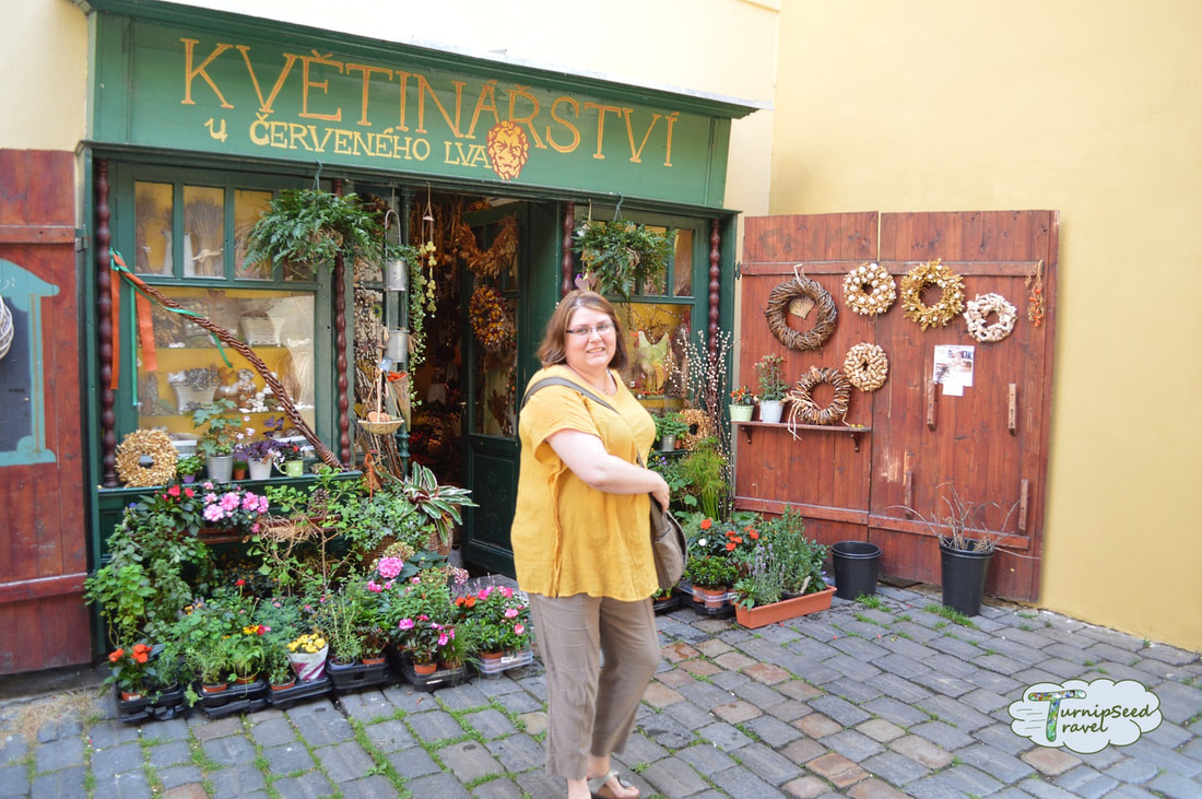 Vanessa wears a yellow top and twirls outside a cute floral shop in Prague