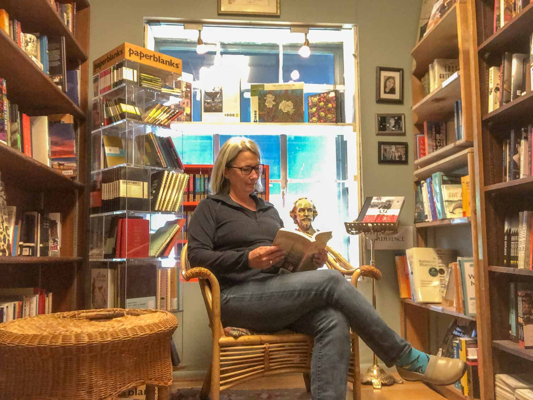 Woman sits on a chair and reads while surrounded by bookshelvesPicture