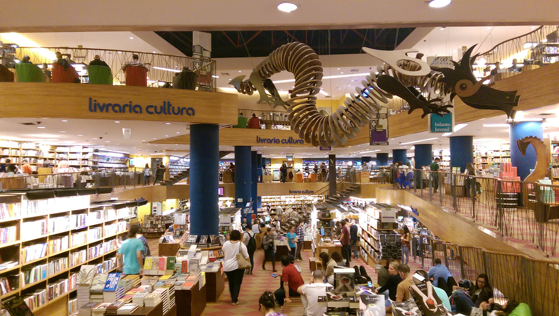 Interior Livraria Cultura from balcony with shelves of books, people shopping, and a large dragon puzzle suspended from the ceiling
