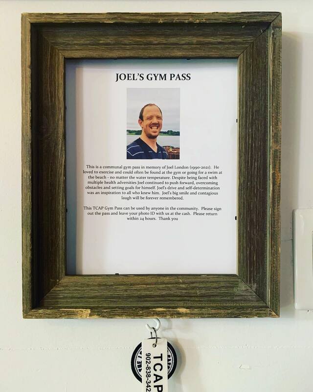 A wooden frame showing the story of Joel's Gym Pass, with a key chain hanging from the bottom.