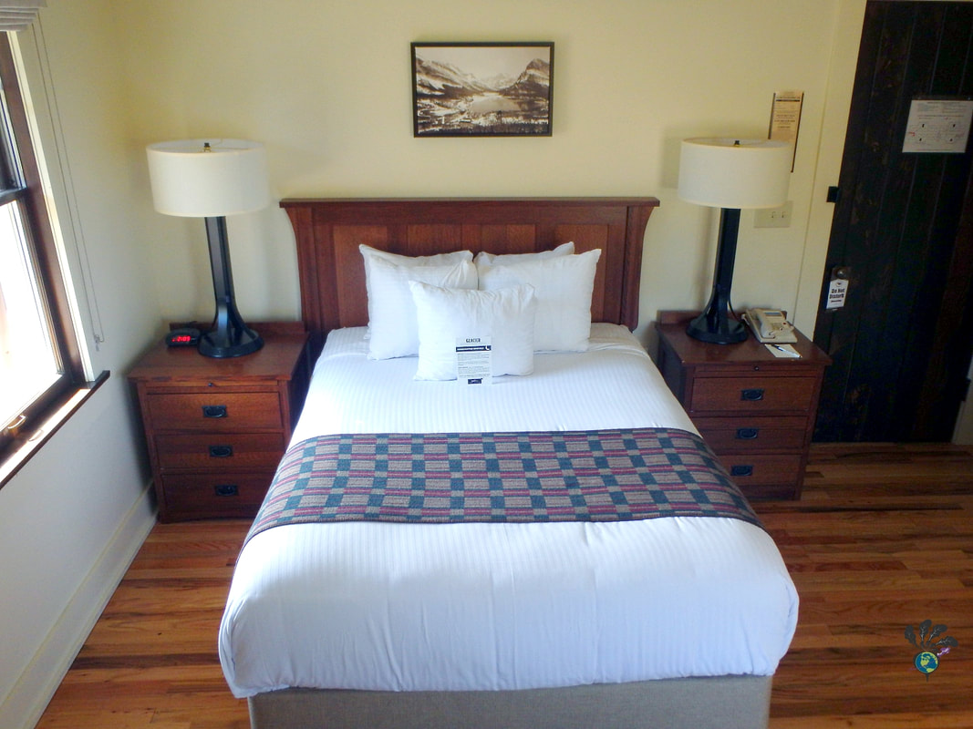 Interior bedroom shot with a queen size bed flanked by two night stands at Many Glacier Hotel Montana Picture