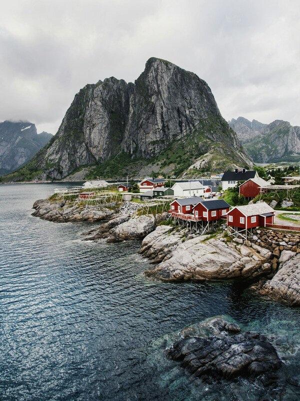 Small red houses on stilts sit at the edge of the water with a mountain in the backgroundPicture