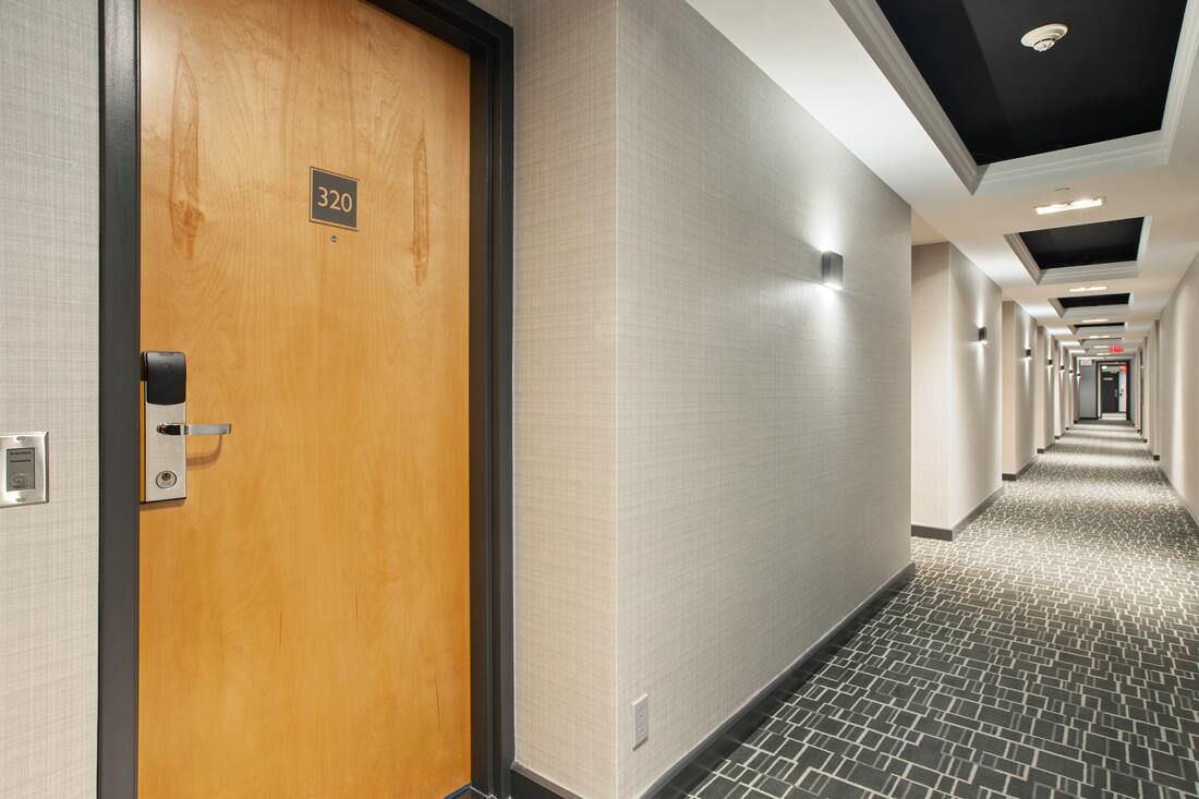 Generic business hotel hallway showing white walls, brown doors, grey patterned carpet, and skylights.