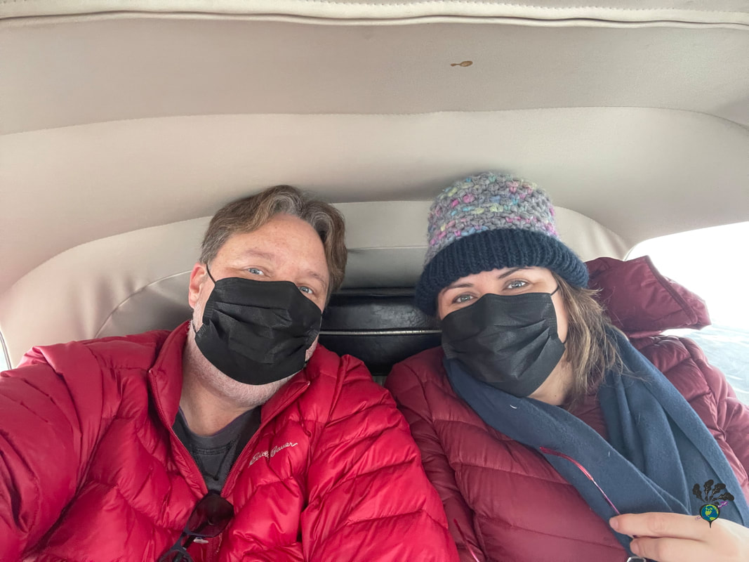 Vanessa and Ryan, both wearing red jackets and black face masks, sit in the snug backseat of the plane