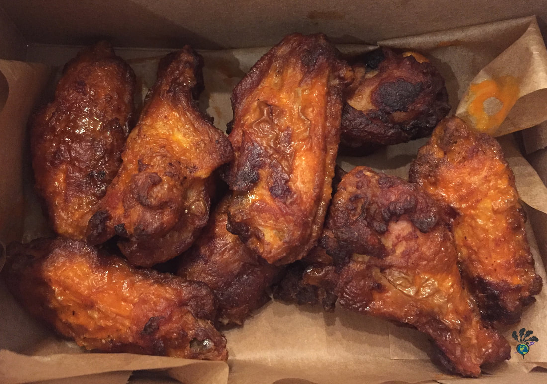 BBQ style chicken wings sit in brown takeout container paper
