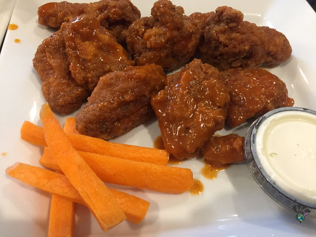 Square white plate holding breaded hot chicken wings from Wild Wing plus a side of carrot sticks and a small plastic take out cup containing ranch dip Picture