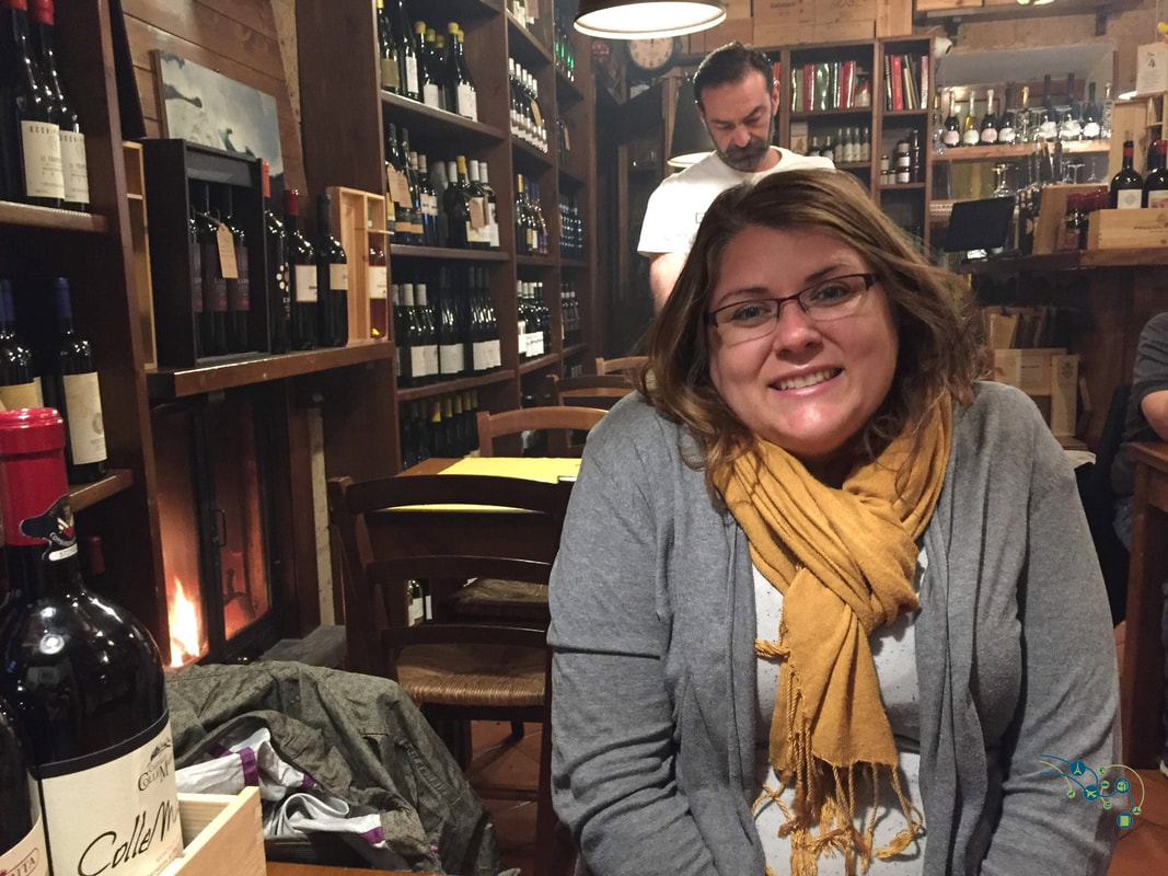Vanessa sits in a cozy wine bar wearing a grey sweater and yellow scarf