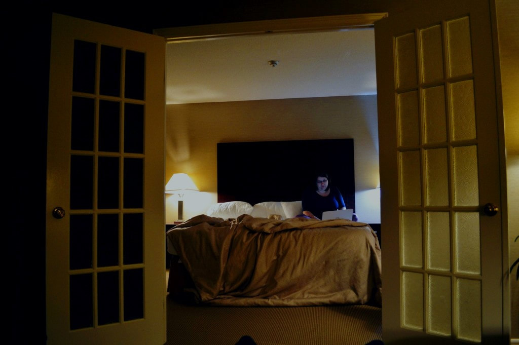 A photo of dusk of Vanessa working in a dark hotel room with packing things on the bed.