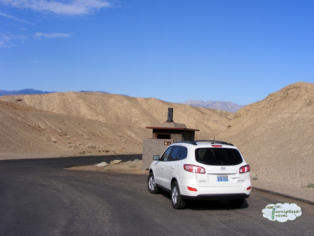 White car next to an outhouse in Death Valley Picture