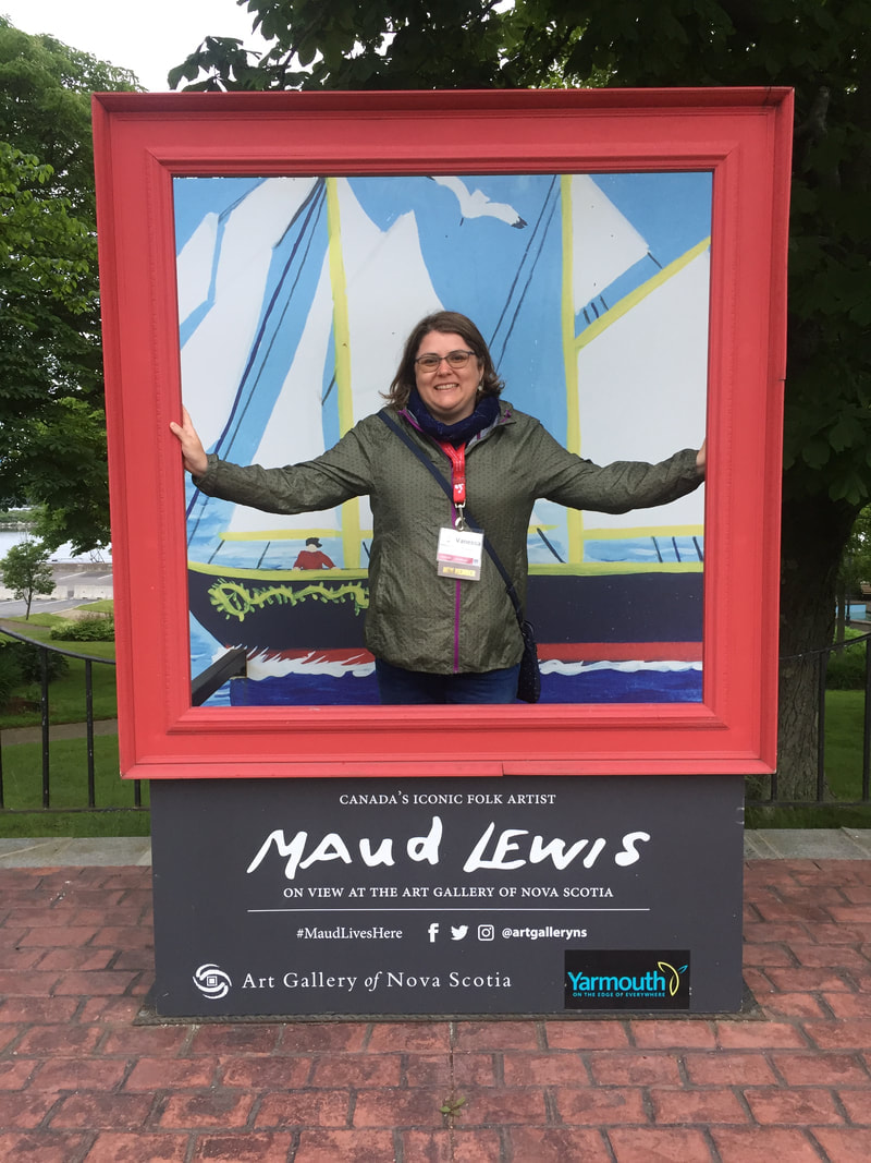 Vanessa stands in a selfie station situated next to a park in Yarmouth, showing a painting by Maud Lewis of the Bluenose ship Picture