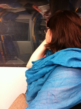 Vanessa stares out a train window while wearing a blue scarf
