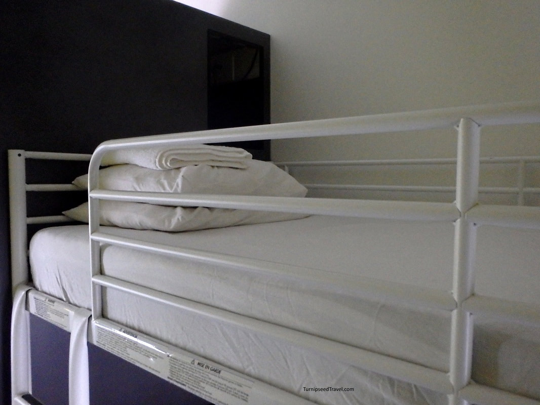 Close up of a top bunk showing white sheets and a towel folded on a pillow