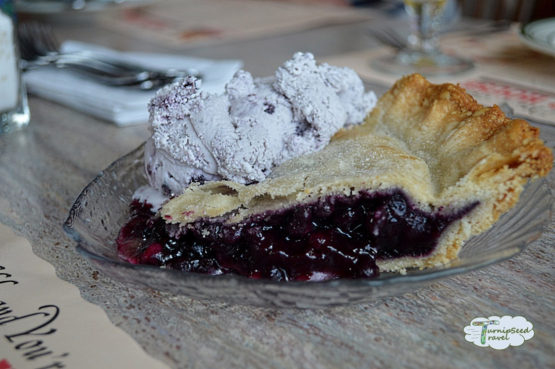 Slice of blueberry pie on a glass plate with a scoop of pale blue blueberry ice cream next to it.Picture