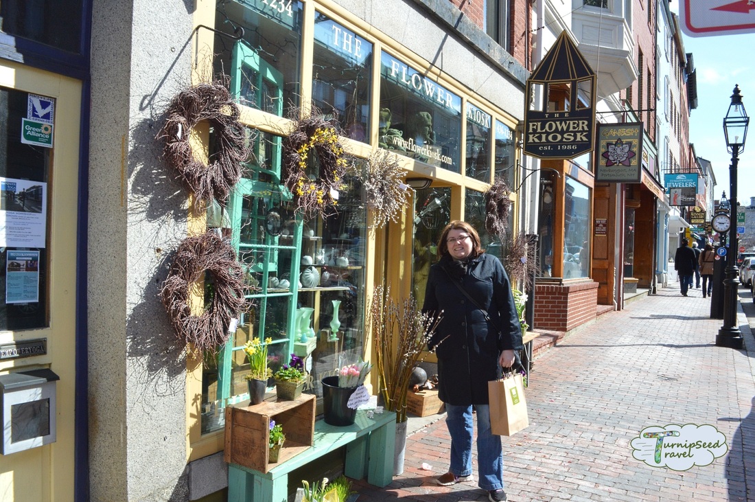 Vanessa wears a black coat and stands next to the Flower Kiosk shop in Portsmouth.