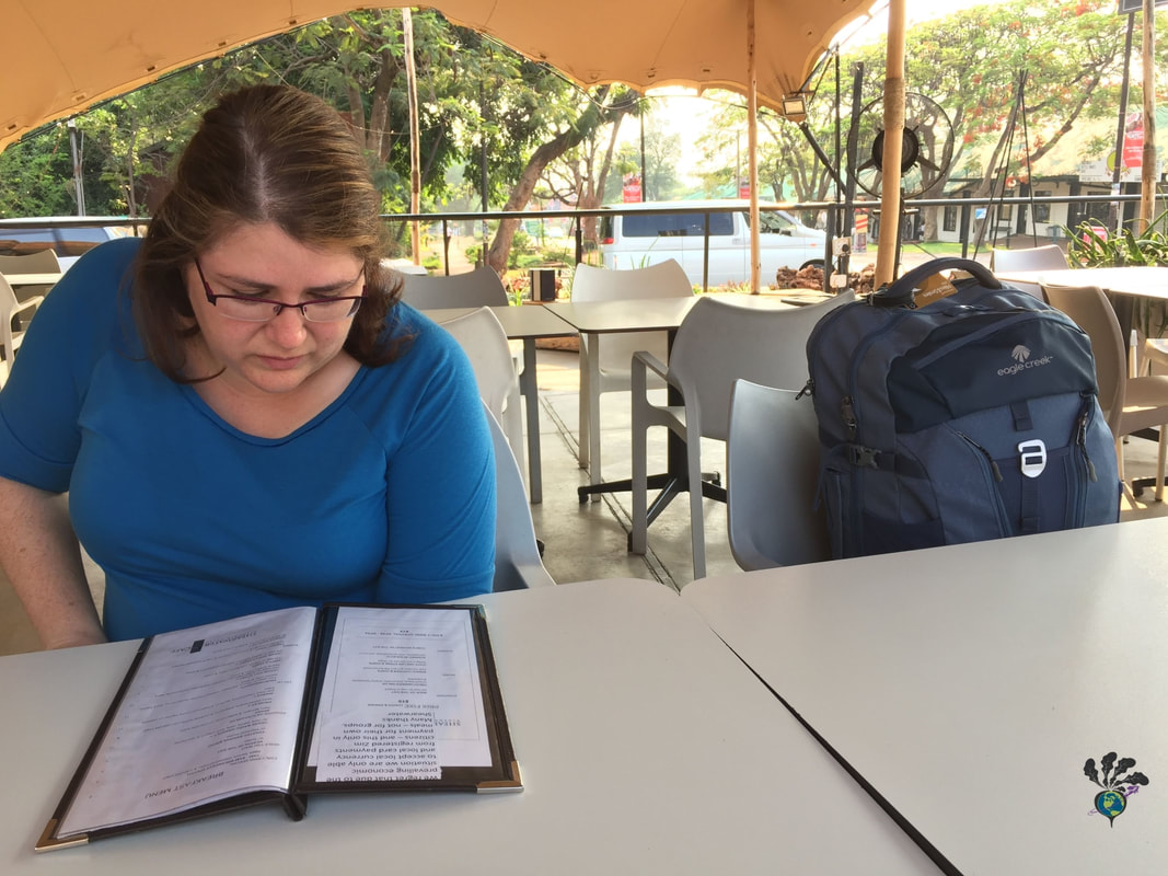 Vanessa studies a menu at an outdoor cafe wearing a blue shirt