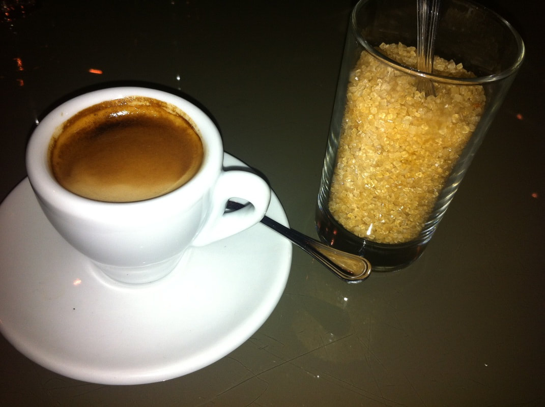 A tiny white espresso cup and a shot glass filled with raw sugar.