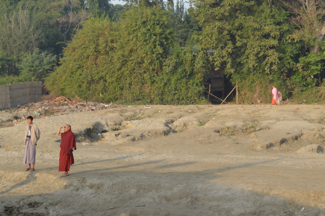 A monk stands on the riverbank wearing red robes Traveling on the Irrawadddy River in Myanmar Mandalay to Bagan