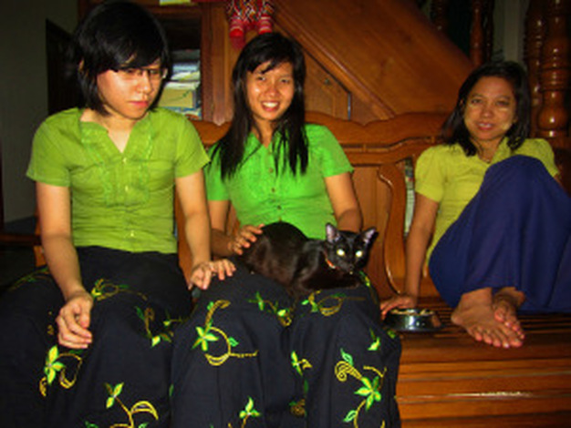 Three women in green and blue uniforms play with a cat