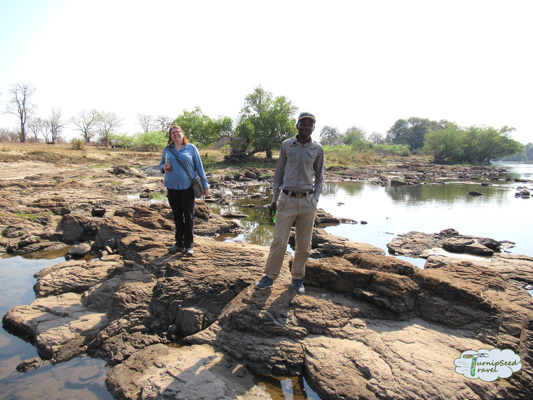 Vanessa and a safari guide stand on the rocks by the river