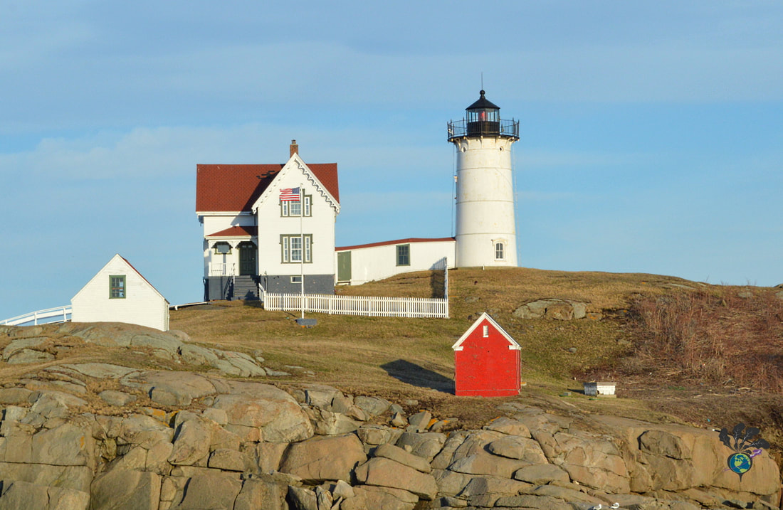 Lighthouse, white home, and small side buildings sit on top of a rocky island.