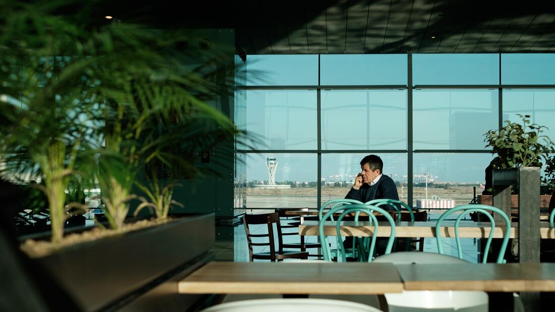 Canadian Transportation Agency Flight Delay Compensation Rules. Traveler sits in an airport at a cafe table surrounded by decorative plants