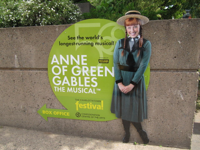 Green sign advertising the show with a life size photo of an actor dressed as Anne