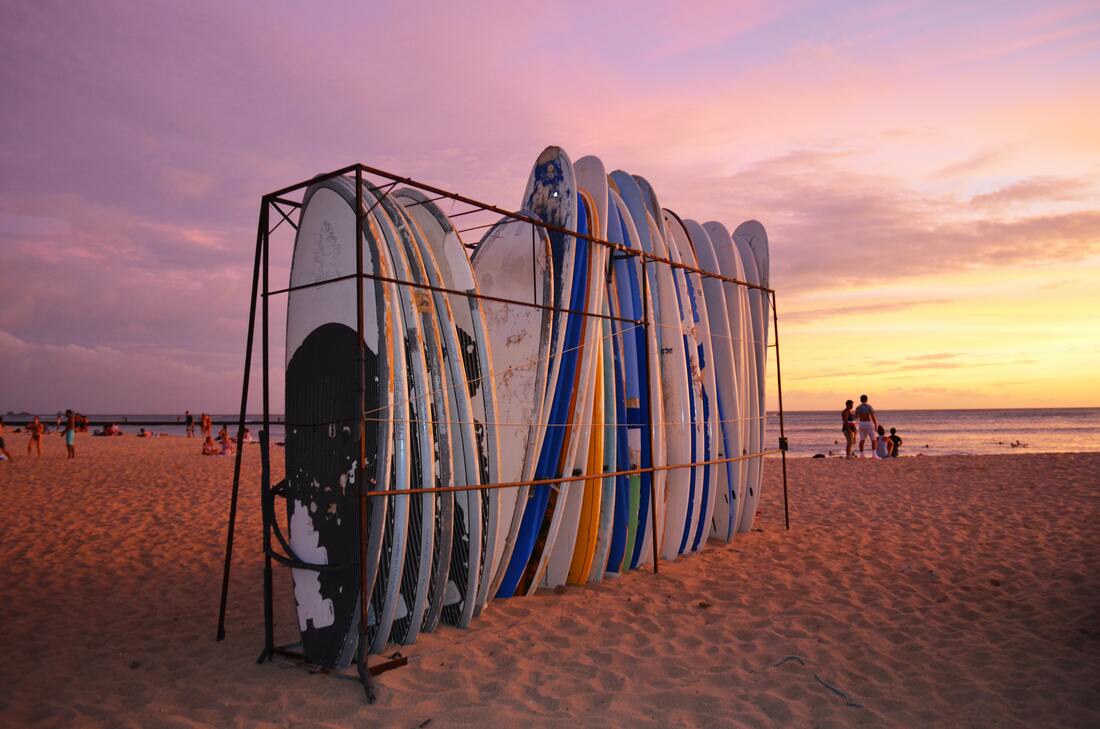 Free things to do in Waikiki: A stand of surfboards at sunset with a pink sky and beach.