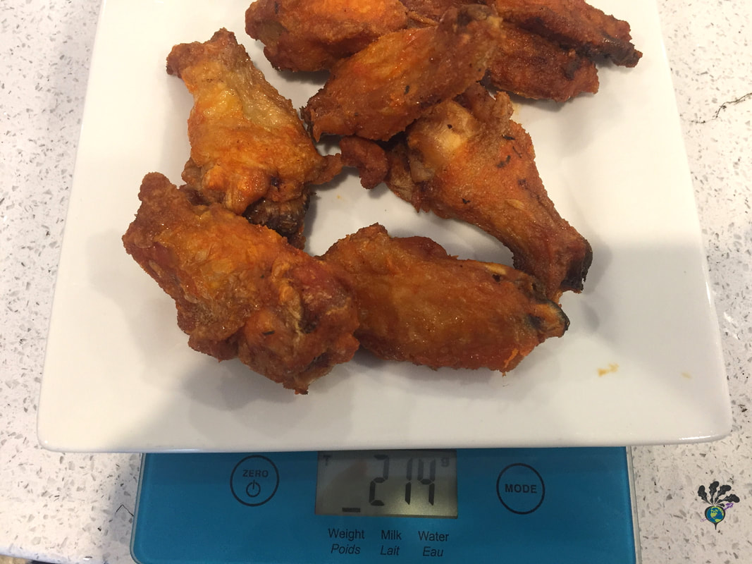 Wings on a white plate being weighted on a blue kitchen scalePicture