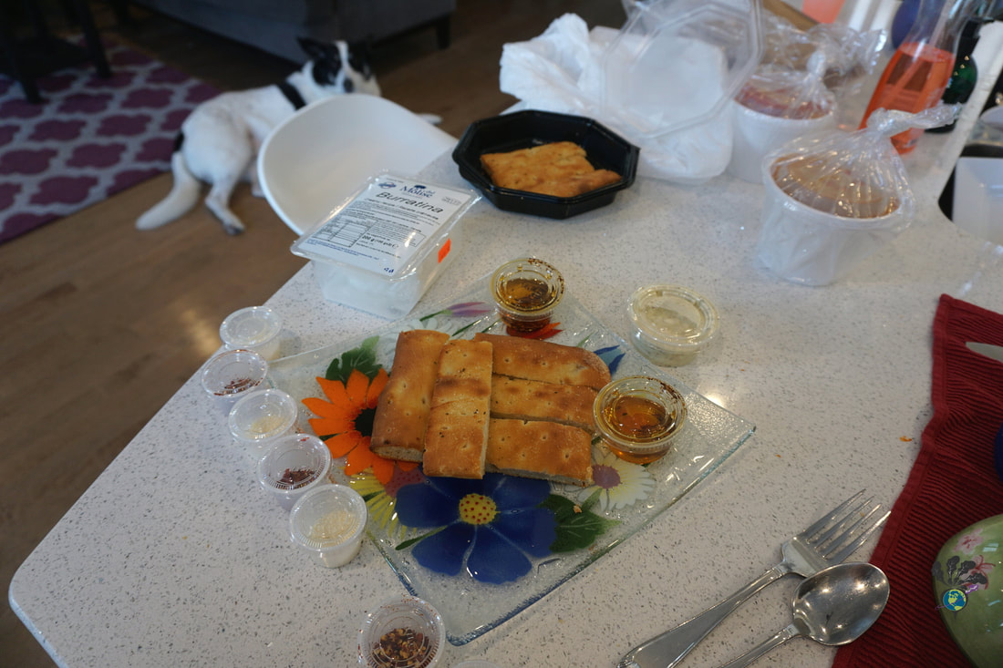 Preparing a plate of breadsticks, buratta cheese, and dips with takeout containers on the counterPicture