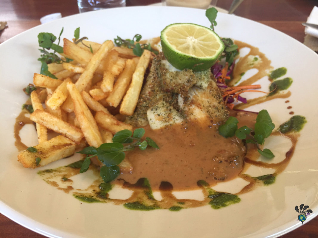 Eating and drinking in Victoria Falls at Dean's Cafe: White plate decorated with swirls of sauce holding fries and fish covered in spicy peanut sauce