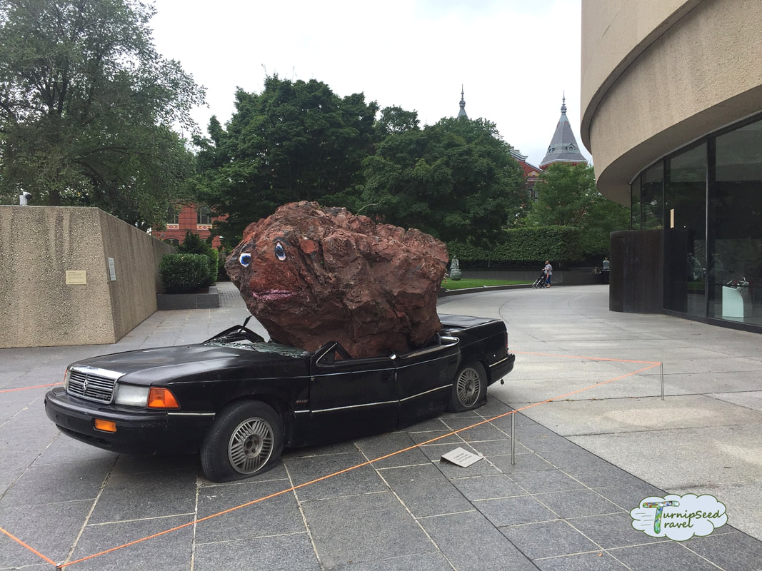 Art display showing a large boulder with painted eyes crushing an old car at the Hirshhorn Museum Picture