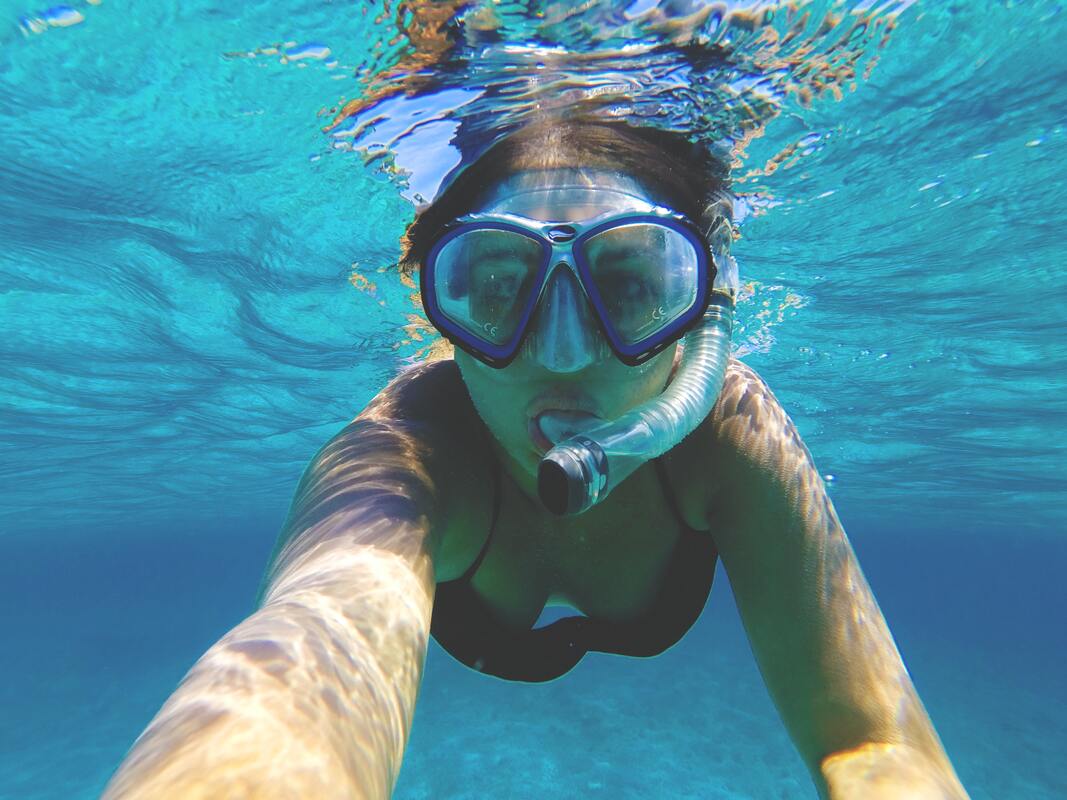 Stock photo of a woman snorkelling in blue water wearing a black swimsuit.