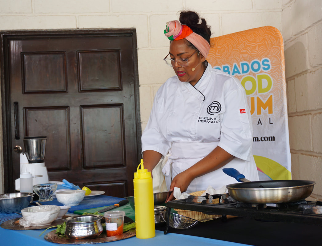Chef Shelina Permalloo stands at a demonstration table wearing a white chef's coat, her hair tied back in a colourful pink scarfPicture