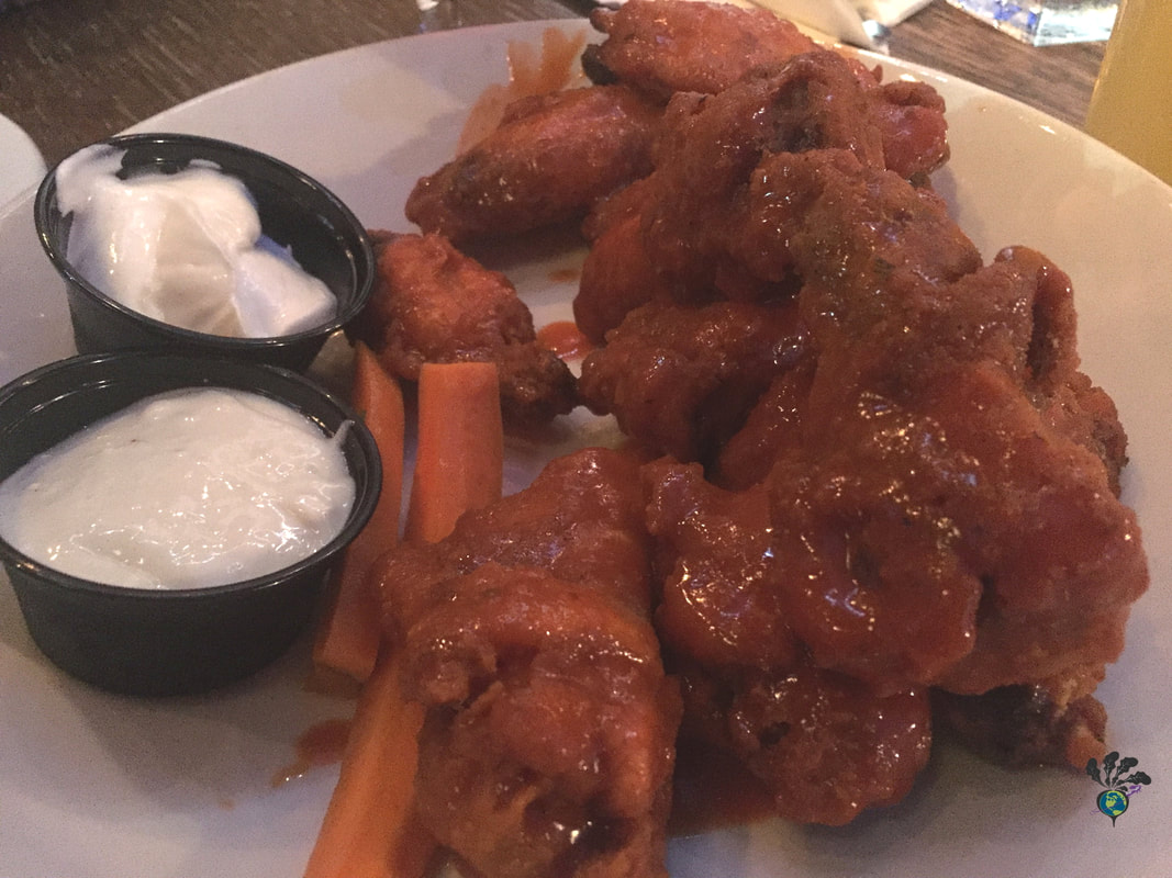 Plate of 10 large hot wings covered in sauce, next to two carrot sticks and two small containers of sour cream dip