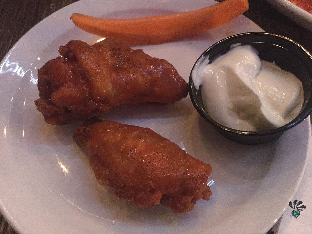 Two hot wings on a white side plate with a carrot stick and black container of sour cream dip 