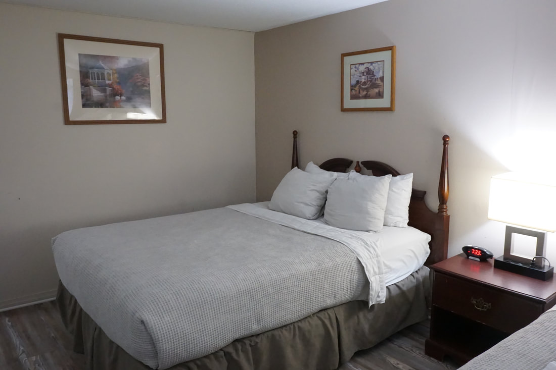 Basic motel room, showing a double bed with white and grey covers and wood furniture.