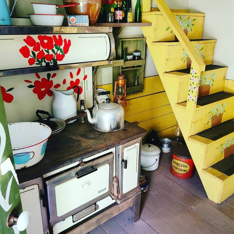 Interior of the tiny house showing yellow stairs painted withe flowers and a white old fashioned stove with red flowers painted on itePicture