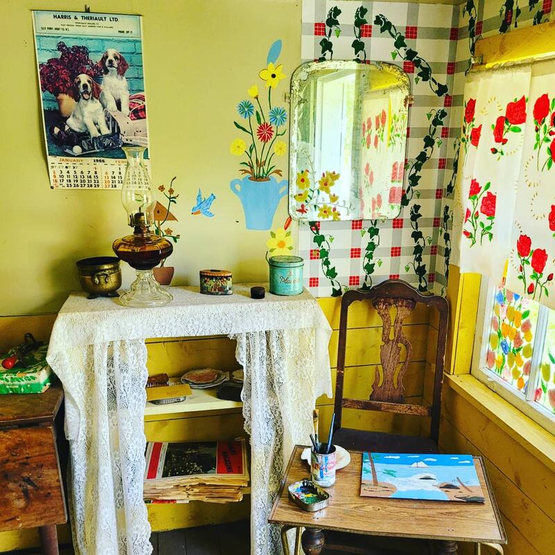 Tiny house interior with yellow walls with painted ivy and flowers and an old fashioned chair set up next to a table with a half finished painting on it.Picture