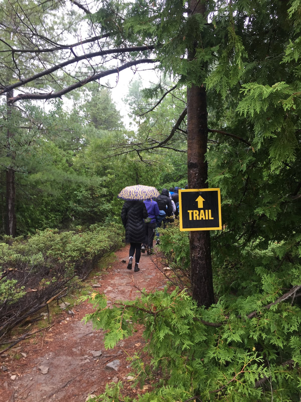 The black and yellow sign marking the start of the trail, with people walking in the distance.