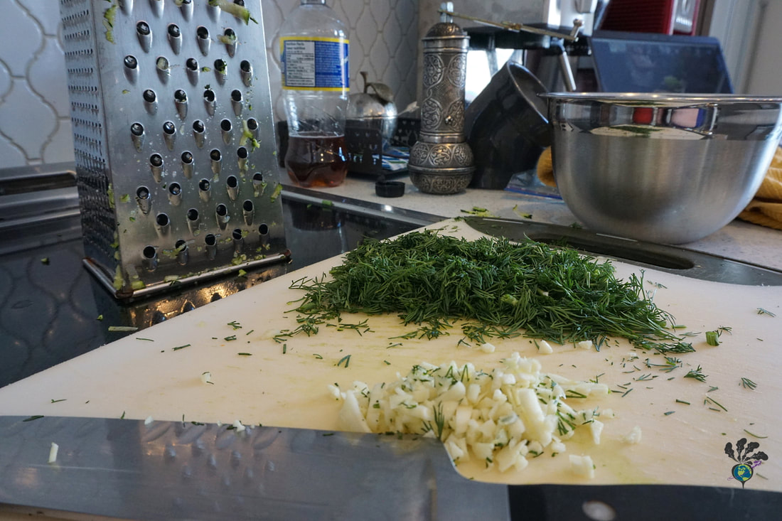 Garlic and dill on a cutting board with grater and bowl in the background 