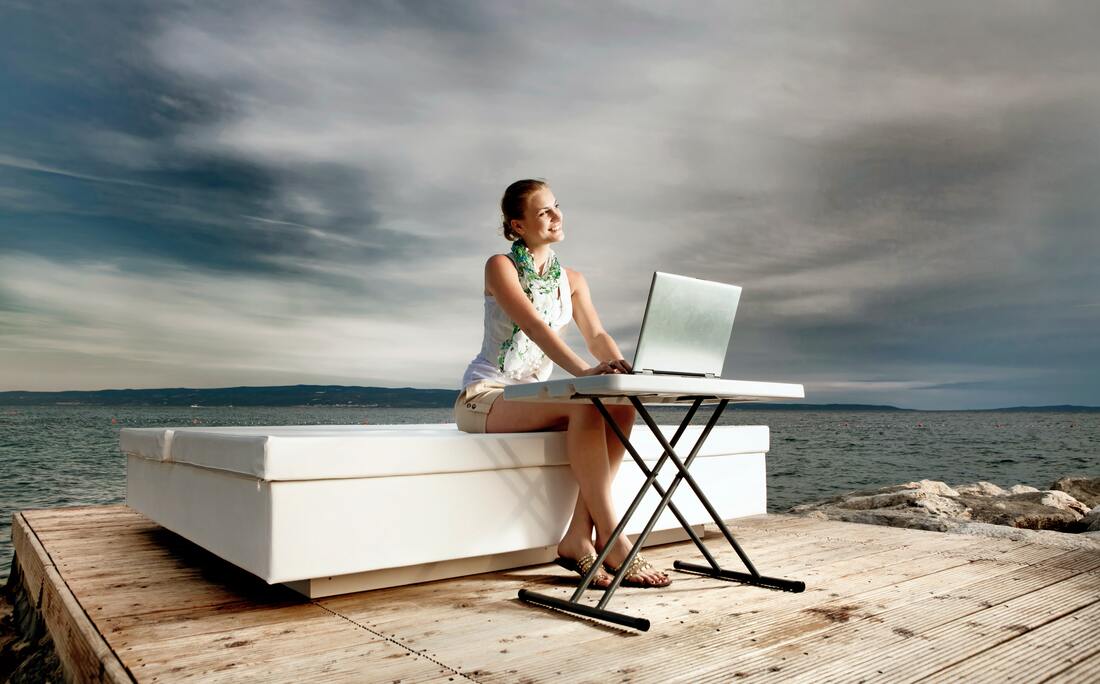 Woman sits on large white platform on a dock, working at a small portable table.Picture
